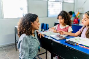 Young teacher woman talking to child student girl during class at school
